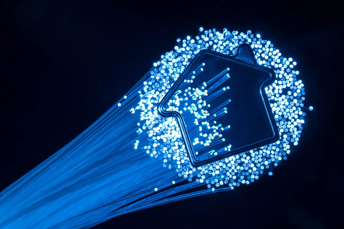 Une icône de maison bleue lumineuse entourée de fibres optiques lumineuses sur fond sombre, symbolisant la connectivité numérique.